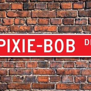 Puede incluir: Señal de calle roja con letras blancas que dice "PIXIE-BOB DR."
