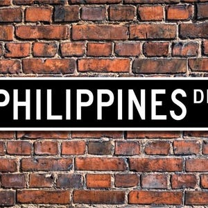 Può includere: Un cartello stradale bianco e nero con il testo "PHILIPPINES DR."