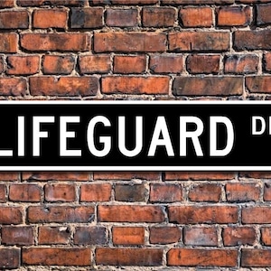 Könnte beinhalten: Ein schwarz-weißes Straßenschild mit dem Text "LIFEGUARD DR." in weißen Buchstaben auf schwarzem Hintergrund.