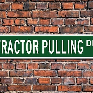 May include: A green and white street sign with the text "TRACTOR PULLING DR." on a brick wall background.