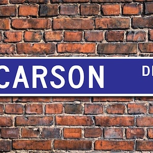 Puede incluir: Un cartel de calle azul con letras blancas que dice "CARSON DR."