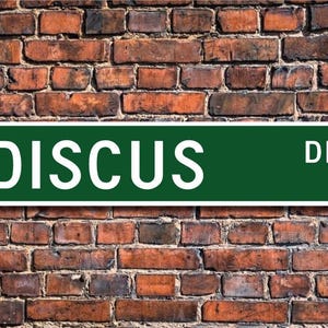 Könnte beinhalten: Ein grünes Straßenschild mit weißen Buchstaben, auf dem "DISCUSS DR." steht.