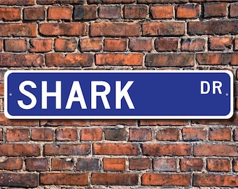 May include: A blue street sign with white lettering that reads "SHARK DR."