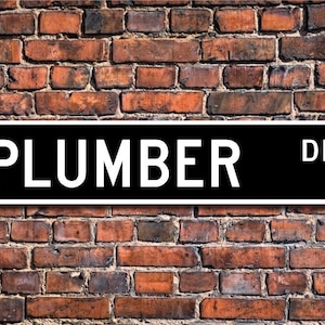 May include: Black and white street sign with the text "PLUMBER DR." in white letters on a black background.