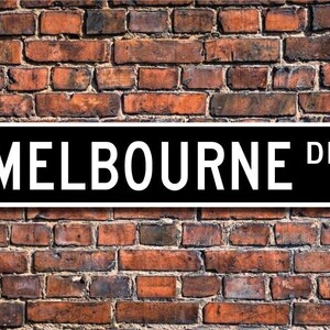 May include: Black and white street sign with the text "MELBOURNE DR." on a brick wall background.