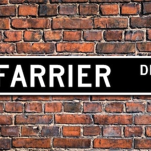 Könnte beinhalten: Ein schwarz-weißes Straßenschild mit dem Text "FARRIER DR." in weißen Buchstaben auf schwarzem Hintergrund.