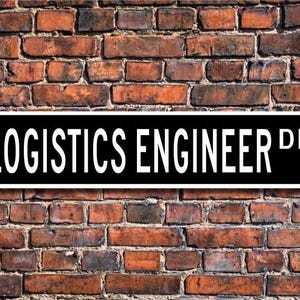 May include: Black and white street sign with the text "LOGISTICS ENGINEER DR." on a brick wall background.