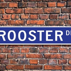 May include: A blue and white street sign with the text "ROOSTER DR." on a brick wall background.