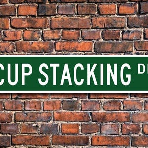 May include: A green street sign with white lettering that reads "CUP STACKING DR."