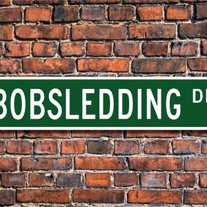 Puede incluir: Un cartel de calle verde con letras blancas que dice "BOBSLEDDING DR."