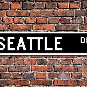 May include: Black and white street sign with the text "SEATTLE DR." on a brick wall background.