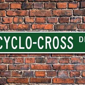 Może przedstawiać: Zielony i biały znak drogowy z napisem "CYCLO-CROSS DR."