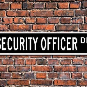 Könnte beinhalten: Schwarz-weißes Schild mit dem Text "SECURITY OFFICER DR." vor einem Hintergrund aus Ziegelmauer.