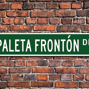 May include: A green street sign with white lettering that reads "PALETA FRONTÓN DR."