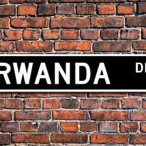 May include: Black and white street sign with the text "RWANDA DR." on a brick wall background.