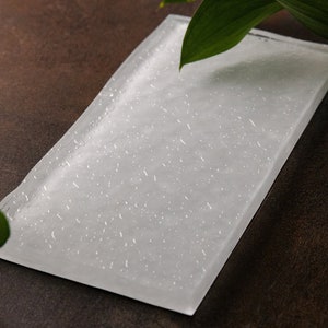 May include: A white rectangular glass serving tray with a textured surface. The tray is on a brown background with green leaves.