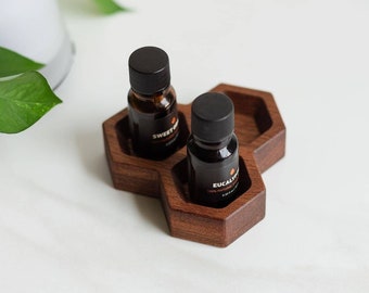 Puede incluir: Dos pequeños frascos de vidrio marrón con tapas negras y etiquetas, colocados en una bandeja hexagonal de madera. Las etiquetas dicen "Sweet Orange" y "Eucalyptus".