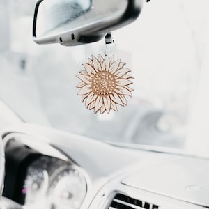 May include: A white wooden sunflower car air freshener hanging from the rear view mirror of a car.