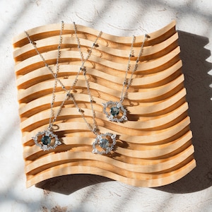 May include: Three silver necklaces with blue gemstone pendants on a wooden display stand. The pendants are surrounded by smaller clear gemstones.