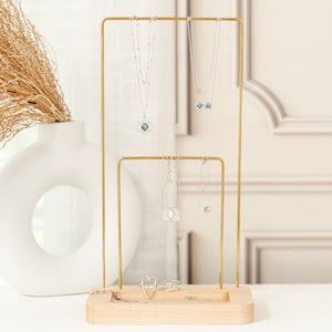 May include: A gold metal jewelry stand with two tiers for necklaces and a bottom shelf for rings. The stand is made of wood and has a natural finish.