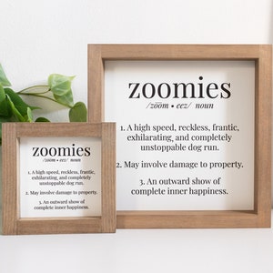 May include: Two square wooden framed signs with white backgrounds and black text. The text reads: zoomies /zoom•eez/ noun. 1. A high speed, reckless, frantic, exhilarating, and completely unstoppable dog run. 2. May involve damage to property. 3. An outward show of complete inner happiness.