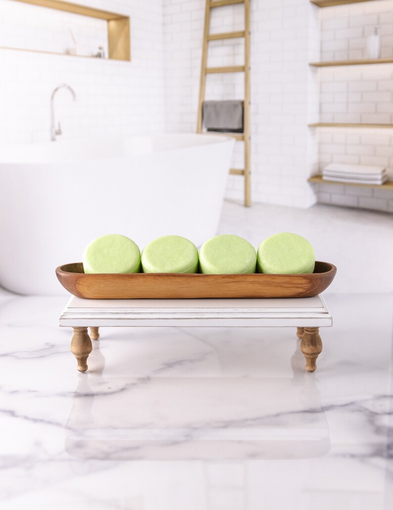 May include: Four green shampoo bars in a wooden tray on a white stand. The tray is on a white marble surface.