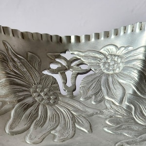 Puede incluir: Una bandeja de metal plateado con un dise&ntilde;o floral. La bandeja presenta girasoles en relieve y un borde festoneado. Las flores est&aacute;n detalladas con p&eacute;talos y hojas. La bandeja probablemente se utiliza para servir o exhibir.