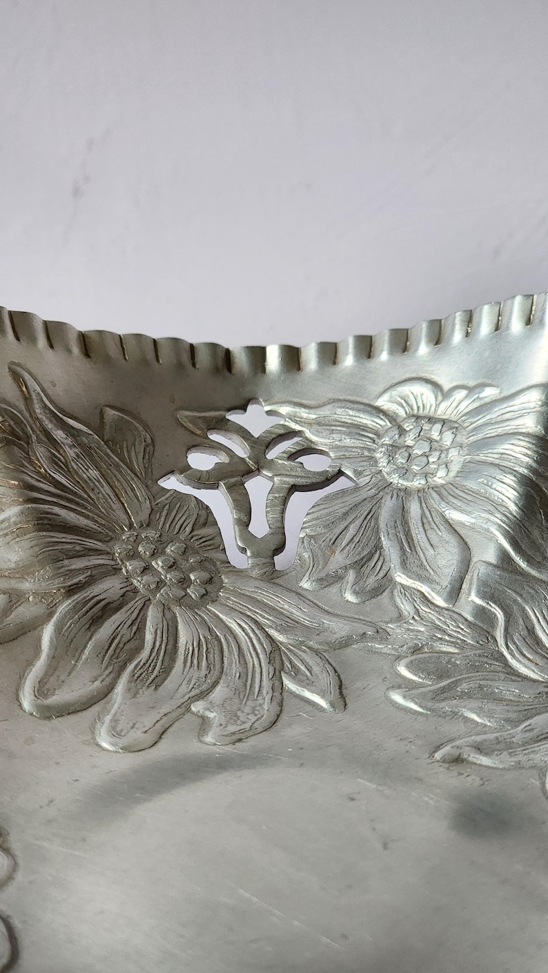 Puede incluir: Una bandeja de metal plateado con un dise&ntilde;o floral. La bandeja presenta girasoles en relieve y un borde festoneado. Las flores est&aacute;n detalladas con p&eacute;talos y hojas. La bandeja probablemente se utiliza para servir o exhibir.