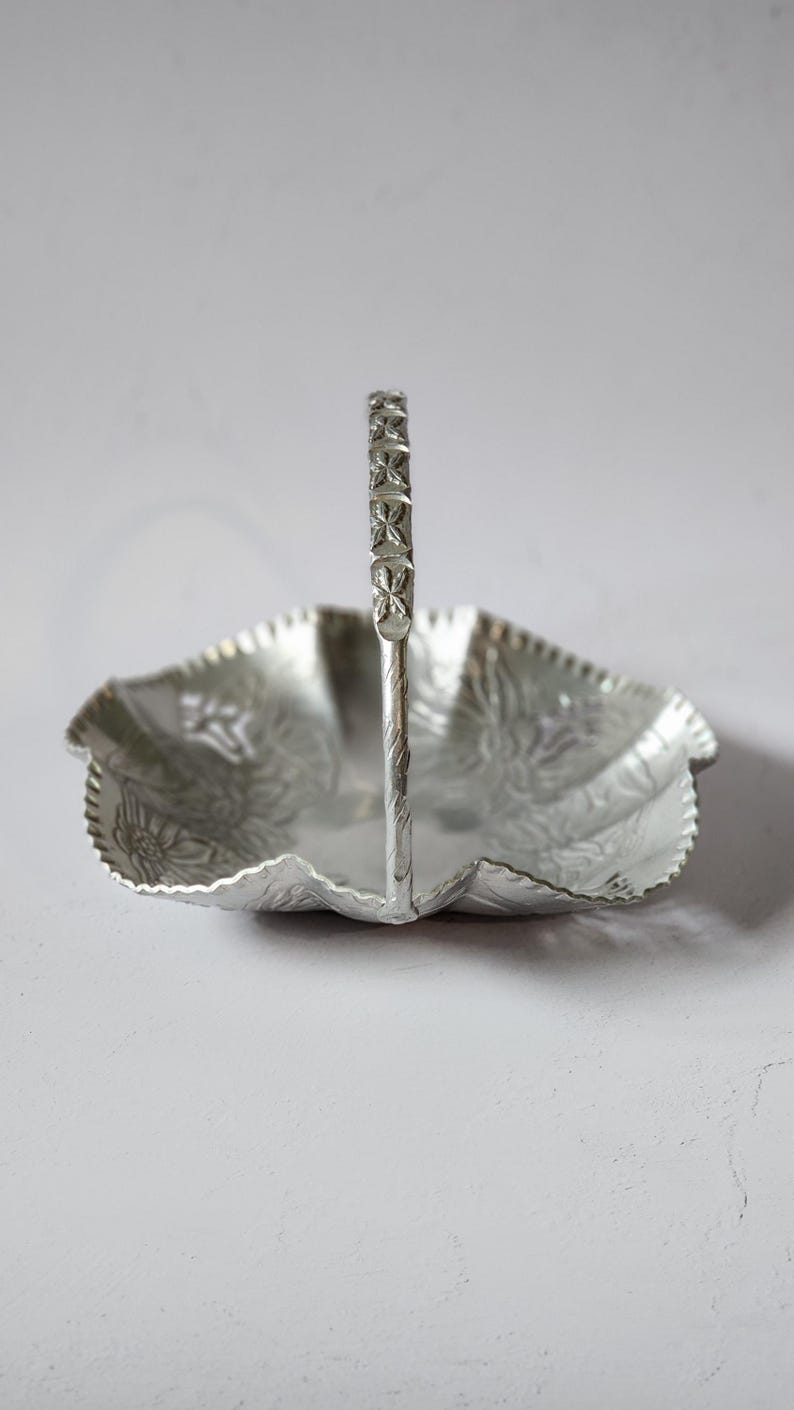 Puede incluir: Plato para servir de color plateado con asa. El plato tiene forma de hoja con borde festoneado y estampado floral. El asa est&aacute; decorada con un dise&ntilde;o geom&eacute;trico. El plato es de metal y es adecuado para servir alimentos.