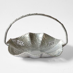 Puede incluir: Una cesta de metal plateado con asa. La cesta tiene un borde festoneado y est&aacute; decorada con dise&ntilde;os florales en relieve. El asa arqueada tiene un acabado texturizado, lo que realza el aspecto decorativo de la cesta. Ideal para servir o exhibir.