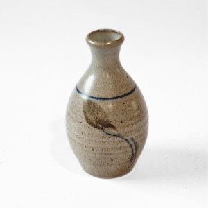 May include: A small, bulbous ceramic vase with a speckled beige and tan finish. The vase features a narrow neck, a flared rim, a thin horizontal blue line encircling the upper body, and a hand-painted dark brown leaf motif on the front surface.