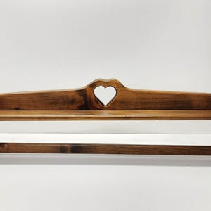 May include: Wooden kitchen shelf with a heart-shaped cutout. The shelf is stained a warm brown and features a lower rod for holding paper towels. The design is rustic and suitable for a country-style kitchen.