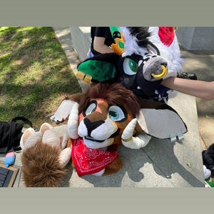May include: A collection of furry animal heads and paws. One head is brown with white horns and a red bandana. Another is black and white with a gold nose ring. A furry paw is also visible.