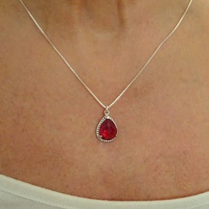 May include: A silver chain necklace with a teardrop-shaped pendant featuring a red gemstone.