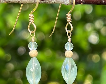 May include: Gold dangle earrings with light green faceted gemstone drops and gold beads.