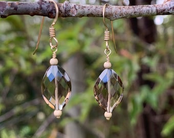May include: A pair of gold earrings with faceted smoky quartz drops. The earrings are hanging from a branch.