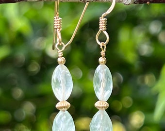 May include: A pair of gold earrings with two light green oval-shaped gemstone beads on each earring.