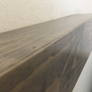 Puede incluir: Un estante flotante rectangular hecho de madera de color marr&oacute;n oscuro con un patr&oacute;n de veta visible. El estante tiene una superficie superior plana y lisa y un borde frontal recto, mostrando la textura natural y los tonos marrones.