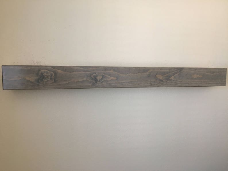 Puede incluir: Un estante flotante rectangular y alargado hecho de madera con un acabado en tono gris. La superficie muestra un patr&oacute;n de veta de madera natural visible con nudos y vetas m&aacute;s oscuras que recorren horizontalmente toda la pieza.