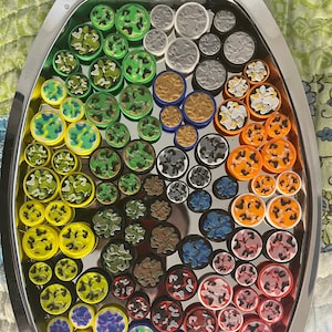 Könnte beinhalten: Eine Sammlung von bunten, gemusterten, runden, plastischen Ohrsteckern in verschiedenen Größen. Die Ohrstecker sind in einem Kreis auf einem silbernen Tablett angeordnet.