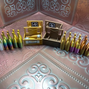 May include: A set of miniature gold and iridescent champagne bottles with two wooden crates. The crates have the text "VIP Celebration" and numbers "1" and "5" on them.