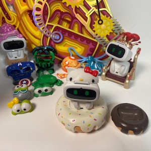 Könnte beinhalten: Eine Sammlung kleiner, farbenfroher Roboterfiguren. Die Roboter haben verschiedene Designs, darunter ein Hello Kitty-Roboter mit roter Schleife, ein Roboter auf einem Donut und Roboter mit Superhelden-Themen. Der Hintergrund zeigt ein farbenfrohes, geschichtetes Kunstwerk.