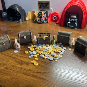 May include: Five small wooden treasure chests with gold and silver coins scattered around them. The chests are closed and have a brown wooden finish with gold accents. There are also small gold and silver vials next to the chests.