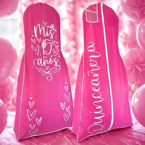 May include: Two bright pink garment bags with white trim. One bag has the text "Mis 15 años" with heart designs. The other bag has the word "Quinceañera" in white script. The bags are designed to protect dresses.