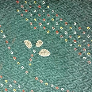 May include: A dark green fabric featuring a subtle geometric weave pattern. The surface is decorated with diagonal rows of small, circular white, yellow, and red dots, along with a central cluster of three light gray, textured, leaf-shaped motifs.