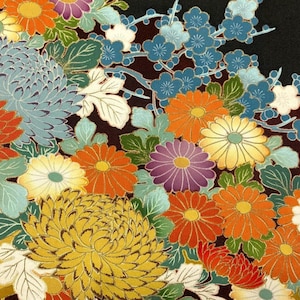 May include: A black fabric surface featuring a dense, colorful floral pattern of chrysanthemums and plum blossoms. The flowers are rendered in shades of orange, yellow, purple, and blue, accented with green leaves and fine gold outlines.