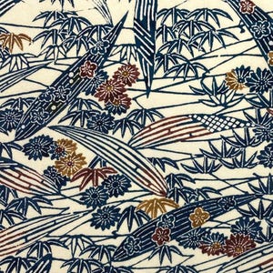 May include: Cream-coloured fabric with a repeating pattern of stylized bamboo, flowers, and leaves in navy blue, brown, and cream. The design features long, curved bamboo stalks and clusters of floral and leaf elements.