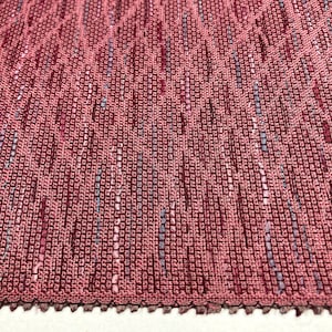 Puede incluir: Primer plano de una tela texturizada con un esquema de color rosa y gris. La tela tiene un aspecto tejido con un brillo sutil.
