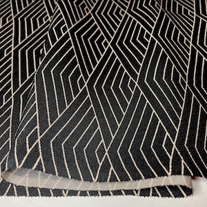 May include: Black and white geometric patterned fabric. The design features a repeating pattern of angular shapes and lines, creating a modern and abstract aesthetic. The fabric is folded, revealing the underside with a lighter color.