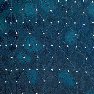 May include: Close-up of a textured fabric with a diamond pattern. The fabric is a deep teal color with white dots at the intersections of the diamond shapes. The pattern is created with white stitching.